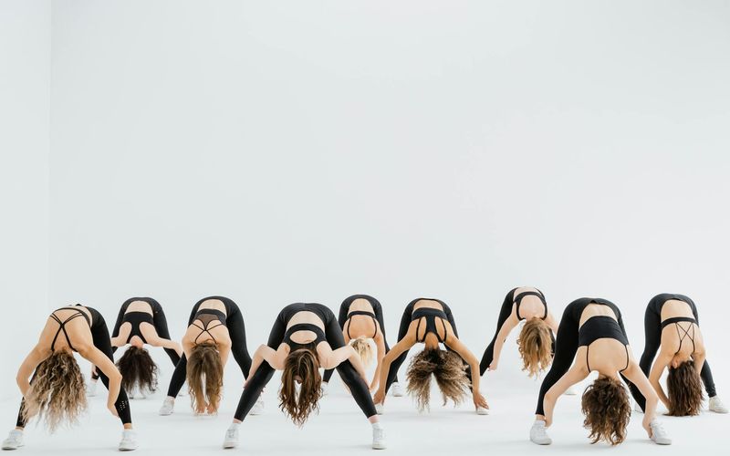A group of people in a bright studio performing a synchronized stretching exercise, smiling.